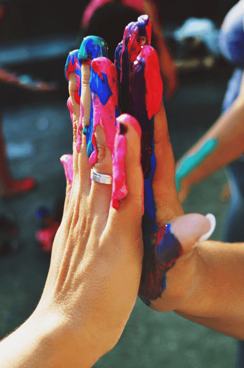 Two hands pressed together with colorful paint smeared, sunlight casting shadows on the skin.