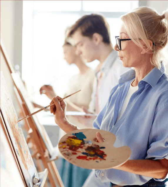 Group of artists painting on easels, focused on their work in a bright studio.