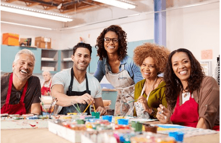 Group of people in an art classroom sitting around a table with various paints and brushes.